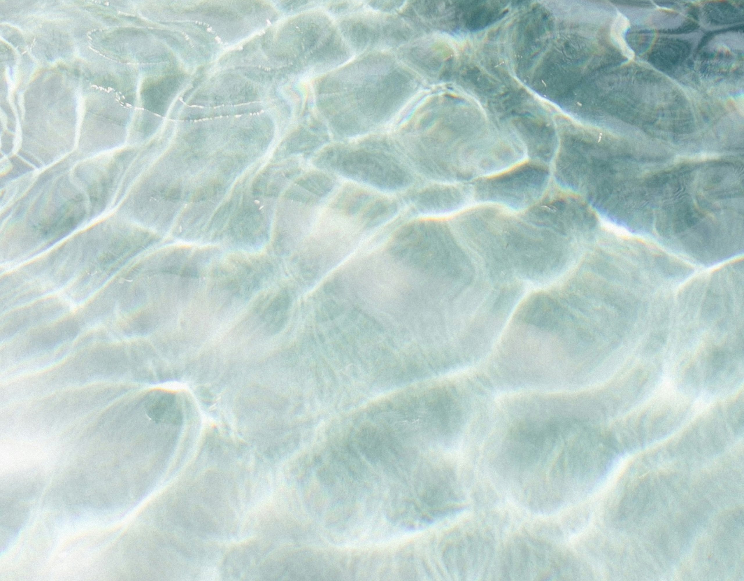 Clear, rippling turquoise water over a shallow, light sandy seabed with sunlight reflecting patterns across the surface.