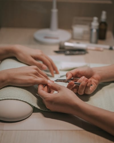 Close-up of a manicurist using cuticle nippers on a client's fingernail during a manicure session at a wooden table.