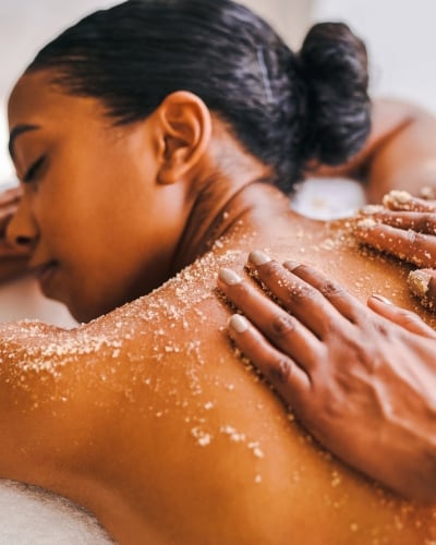 Close-up of a woman receiving a relaxing back scrub treatment with granular exfoliant in a spa setting.