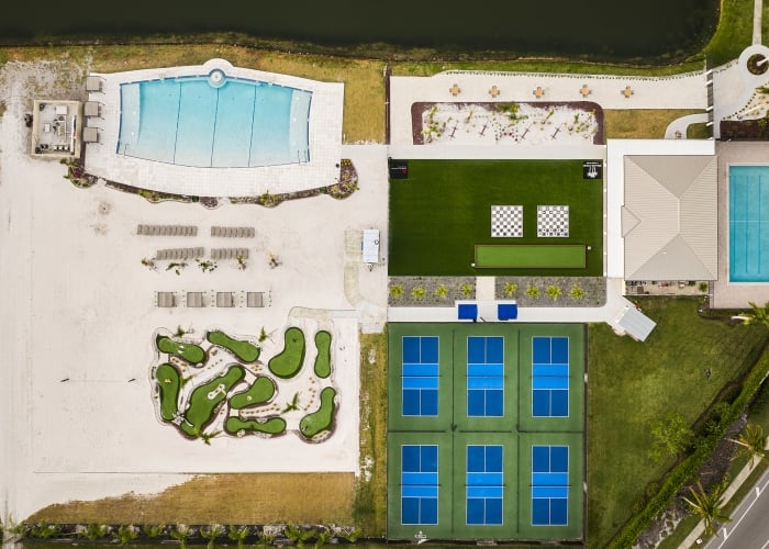 Aerial view of a recreational complex featuring two swimming pools, pickleball courts, a putting green, and a large sandy area with mini-golf holes.