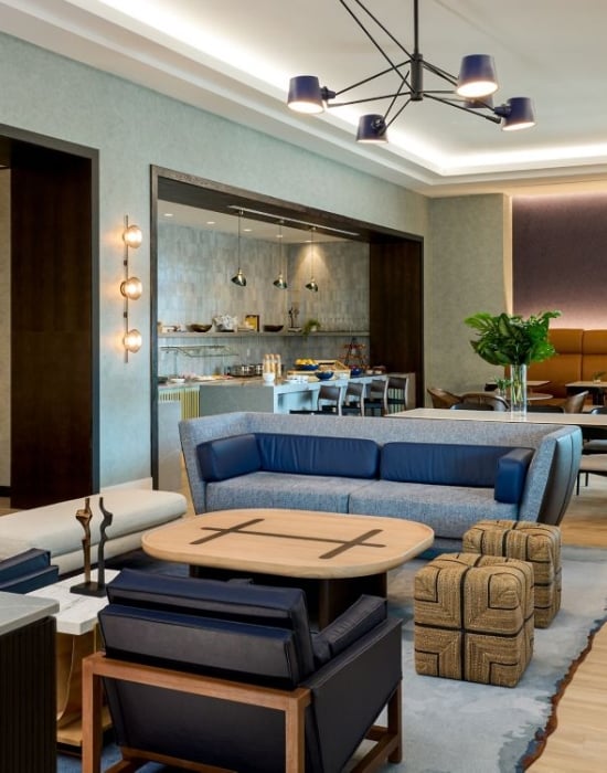 M Club featuring varied seating areas, including blue sofas, leather armchairs, and banquette dining, with a view into a self-service refreshment area.
