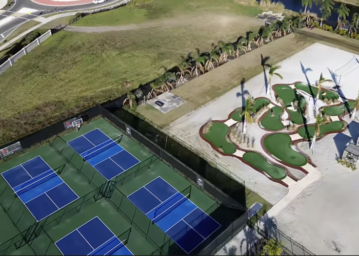 Aerial view of adjacent pickleball courts with blue surfaces and an elaborate miniature golf course set in a sandy area with palm trees.