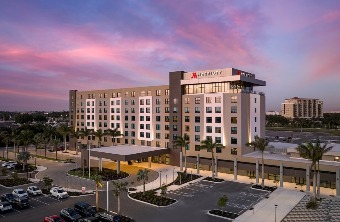 Exterior view of a modern Marriott hotel building at twilight with a vibrant pink and purple sunset sky and surrounding palm trees.