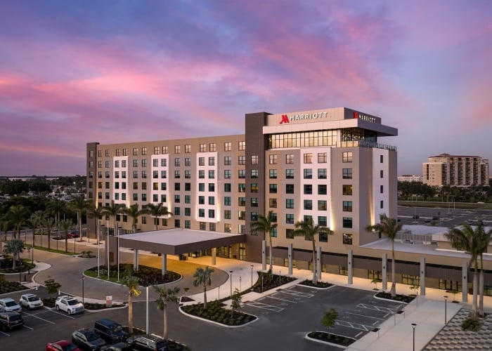 Exterior view of a modern Marriott hotel building at twilight with a vibrant pink and purple sunset sky and surrounding palm trees.