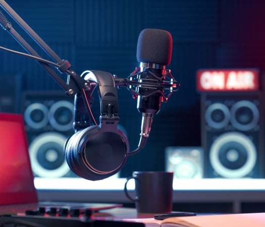 Studio microphone setup with professional headphones hanging nearby, set against a backdrop featuring an "ON AIR" light and studio monitors.