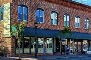 Street-level exterior view of Central Cafe, housed in a historic multi-story brick building with arched windows, a blue awning over the storefront, and small palm trees on the sidewalk.