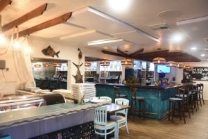 Interior view of the Clam House Bar & Grill featuring a rustic wooden bar with turquoise paneling, woven pendant lights, and indoor seating.