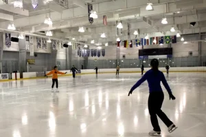 Interior view of skaters on the indoor ice rink at the Ellenton Ice and Sports Complex, with banners hanging from the ceiling.