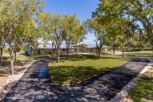 Exterior view of The Venue at Hidden Acres featuring a long paved, curved driveway surrounded by green lawns and large oak trees draped with Spanish moss.