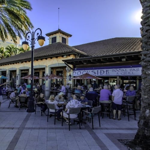 Crowded outdoor patio of Dockside Social Bar & Grill on a sunny day, with patrons seated at tables under umbrellas and an awning.
