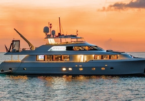 A luxury yacht cruising on calm water during a vibrant golden hour sunset with a glowing orange sky.