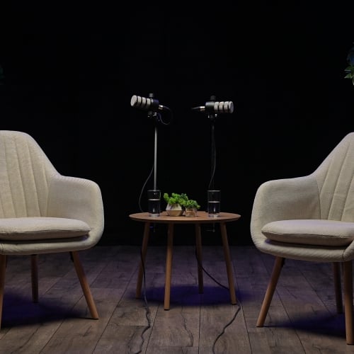 Two stylish chairs face each other in a cozy podcast studio, ready for an engaging interview. Microphones stand poised, and warm lighting sets the tone for inspiring conversations.