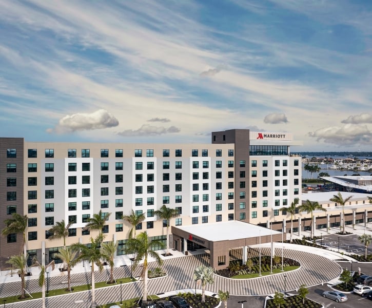 A high-angle exterior view of the modern, multi-story Palmetto Marriott Resort & Spa building on a bright day, featuring palm trees lining the circular driveway and the resort grounds.