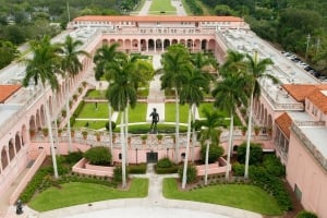 High-angle view of the pink, Italianate courtyard at The John and Mable Ringling Museum of Art featuring tall palm trees, statues, and manicured lawns.